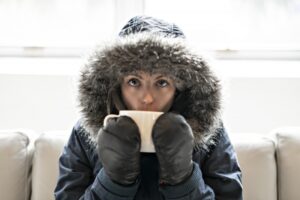 person-indoors-in-coat-hood-and-mittens-with-cup-of-hot-tea