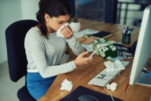 person-at-desk-trying-to-work-blowing-their-nose-and-surrounded-by-tissues